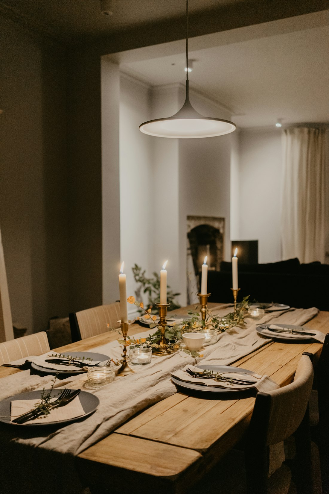 A long wooden dining table laid with candles and linen under a soft pendant light