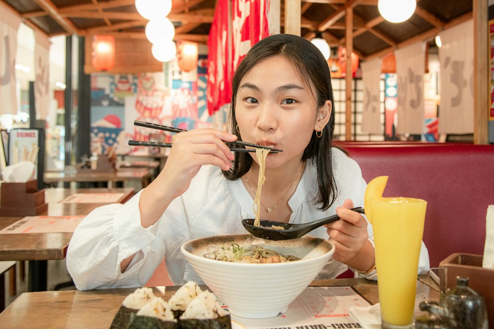 A woman eating a bowl of ramen with chopsticks