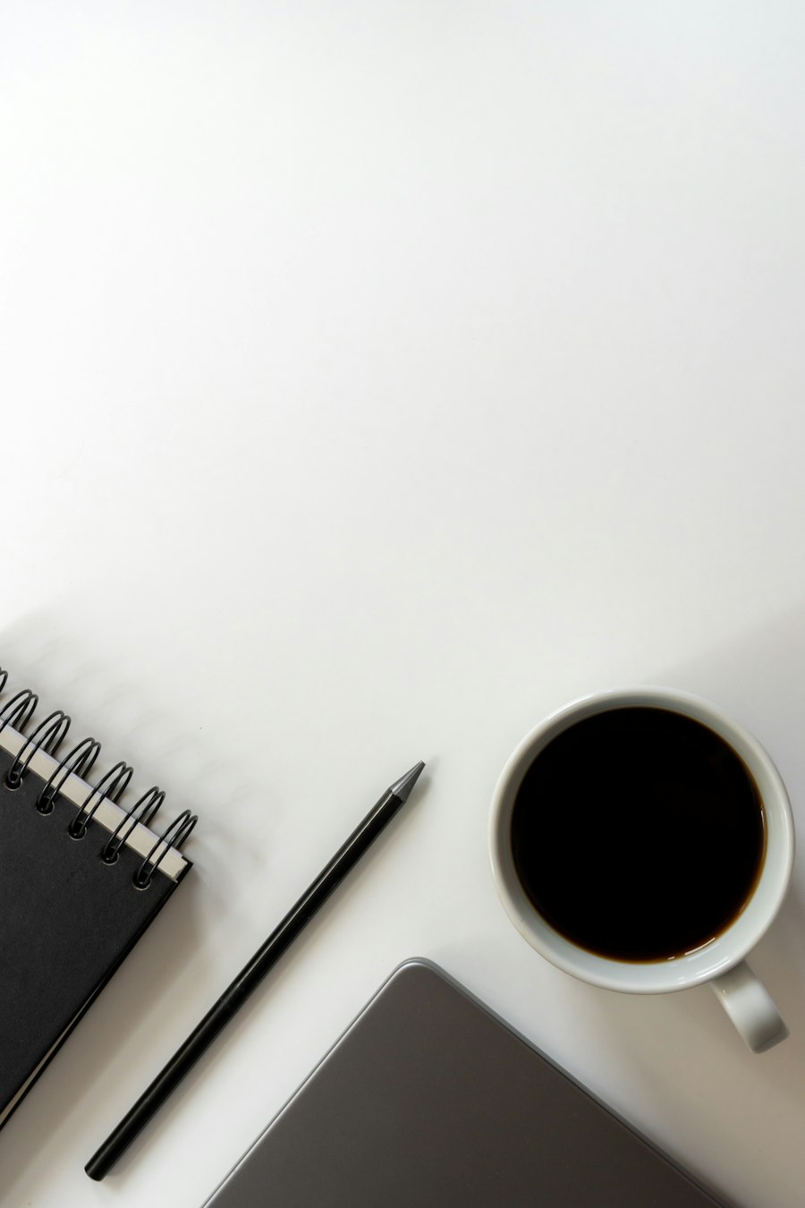 A notebook, pencil and coffee on a clear white desk