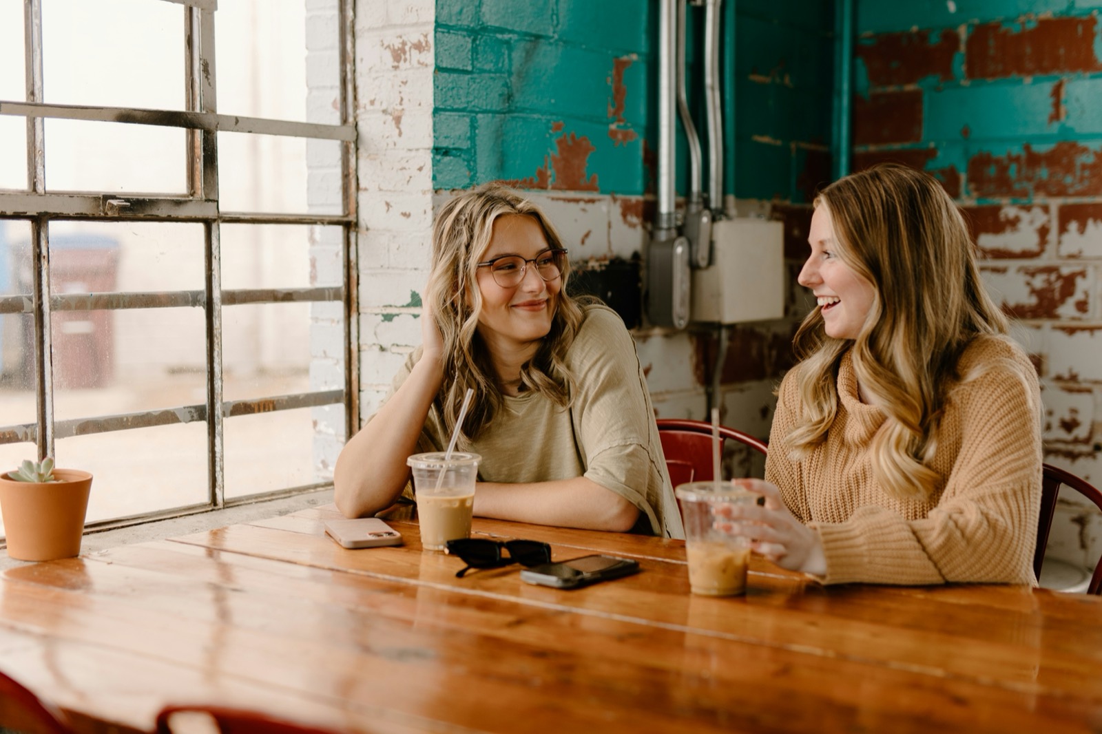 Two women laughing together at a wooden café table