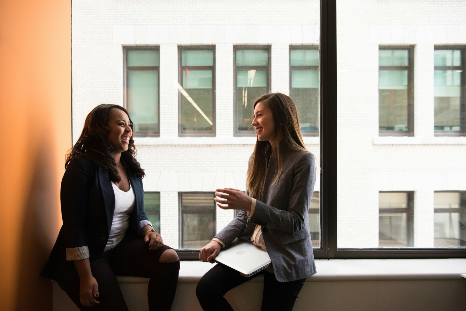 Two women laughing together on a wide window ledge